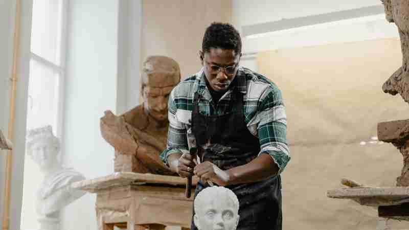 African American sculptor focused on shaping a clay bust in a bright, modern art studio., tags: das handwerk tradition - pexel
